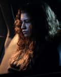 Person with curly hair sitting in a dimly lit car, looking contemplative.
