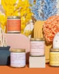 Colorful candles with playful labels surrounded by vibrant yellow, blue, and peach dried flowers on a decorative setup.