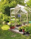 Glass greenhouse surrounded by lush greenery and potted plants on a wooden deck.