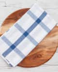 Wooden cutting board with a blue and white checkered cloth on a light wooden surface.