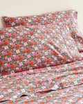 Floral-patterned bed sheets and pillowcases with pink, red, and green flowers on a bed.