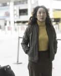 Woman in a yellow turtleneck and green jacket standing at an airport terminal.