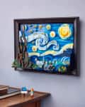 Framed LEGO art of Van Gogh's Starry Night on a wall above a wooden table with books and a potted plant.