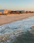 Ocean waves crashing on a sandy beach with beachfront houses at sunset.