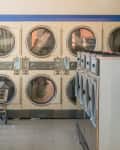 Laundromat interior with rows of front-loading washers, dryers, and a blue folding table.