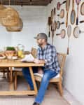 Couple enjoying breakfast at a wooden table in a sunroom with wicker chairs and vintage tennis rackets on the wall.