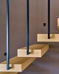 Floating wooden staircase with black metal railings against a brown wall.