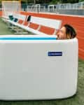 Person in a portable ice bath on a sports field next to a bench, with a cooling unit labeled "Inergize."