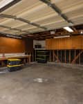 Empty garage with open door, workbench, and storage bins on concrete floor.
