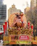 A large turkey float adorned with colorful decorations and performers, parading at the Macy's Thanksgiving event.
