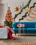 Living room with a blue sofa, Christmas tree, star decorations, gifts, and candles on a mantel.