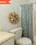 Small bathroom with floral shower curtain, white bathtub, toilet, and seashell wreath on the wall.