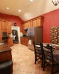 Kitchen with red walls, wooden cabinets, stainless steel fridge, and floral upholstered dining chairs around a round table.