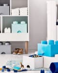 Children's playroom with large blue and gray storage blocks, toys, and folded clothes on white shelves.