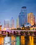 Cityscape at dusk featuring a traditional pagoda, illuminated bridge, and modern skyscrapers reflecting in the water.