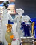 Porcelain figurines in traditional attire displayed among colorful vases at a market stall.