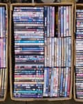 Three cardboard boxes filled with assorted DVD cases, showcasing various movie titles.