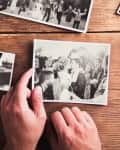 Hands holding a black and white wedding photo on a wooden table with other scattered photos.