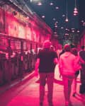 Crowd walking down a narrow alley illuminated by red lights, with graffiti on brick walls.