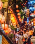 Crowded street with red lanterns and signs, people walking down narrow stairs in a vibrant night market.