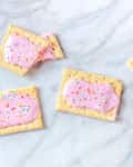 Frosted pink pastries with colorful sprinkles arranged on a marble surface.