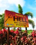 Sign welcoming visitors to Hell, featuring palm trees and colorful foliage in the foreground.