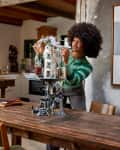 person putting together LEGO model of Gringott's Bank on large wood table
