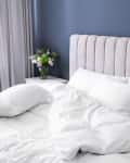 Beige upholstered headboard with white bedding, pillows, and a bedside table with a vase of flowers.
