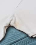 White T-shirt with a yellow stain on the armpit area, placed on a blue wooden surface.