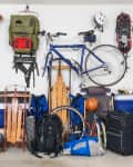 Garage storage with a blue bike, backpacks, sleds, a basketball, and suitcases neatly organized against a wall.