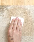 Overhead view of a hand dabbing a coffee stain out of a carpet with paper towel.