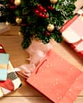Overhead shot of an assortment of wrapped presents on a light wood surface, underneath a small decorated tree.