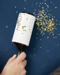 Angled view of a hand holding a lint roller and using it to clean up glitter on a chair cushion.