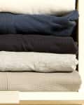 Rolled shirts in a drawer, organized by color: white, navy, black, gray, and beige.