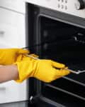 Person wearing yellow gloves placing a rack into a stainless steel oven.