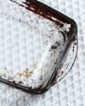 Dirty glass baking dish with food residue on a textured surface.