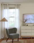Living room with white walls, tall windows with white curtains, white dresser under TV instead of media console