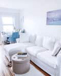 White sectional sofa in a bright room with a blue chair, desk, and wall art saying "Ocean air, salty hair."