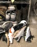 Shoes and boots are unorganized under a shelf.