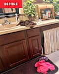 Bathroom vanity with double sinks, wooden cabinets, a potted plant, and towels on the counter; clothes on the floor.