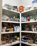 Pantry shelves filled with various food items, jars, containers, and kitchen supplies, organized with a door partially open.