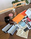 A wooden table with various items including jars, boxes, and bags, alongside a plant and chairs.