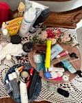 Cluttered vanity table with various skincare and beauty products, towels, and decorative flowers on a lace tablecloth.