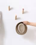 Hand placing a straw hat on a wall with colorful wooden pegs, one holding a white cloth.