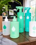 Collection of Safely cleaning products on a wooden table with a potted plant and window in the background.