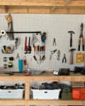 Organized garage pegboard with tools, including hammers, pliers, and screwdrivers, above a wooden workbench with storage bins.