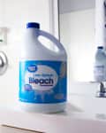 Bleach bottle on bathroom counter near sink and shower with curtain.