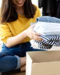 A woman sitting on the floor, putting clothes into a cardboard box for donation