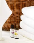 Lavender and lemon essential oil bottles on a white surface with folded towels and a wicker basket.
