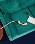 Teal sofa with a pink rotary phone, notepad, and nail polish on a wooden side table.